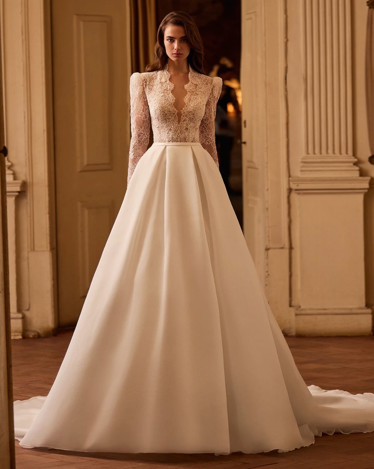 A woman posing in a lace-bodice white wedding dress with a full satin skirt.