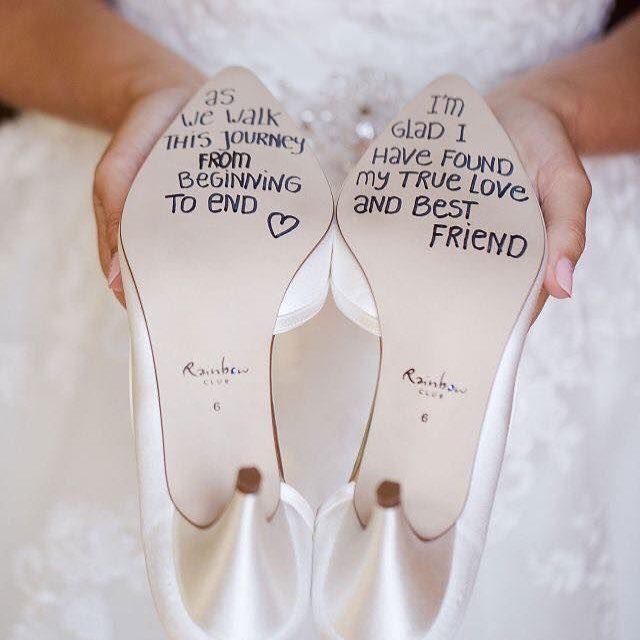 White satin wedding shoes held up showing handwritten romantic messages on the soles.