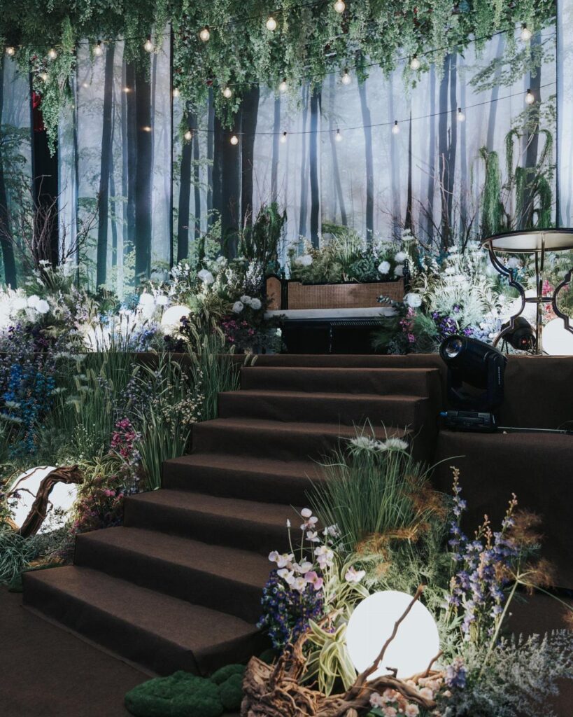 Dark stairs surrounded by lush greenery, wildflowers, and glowing orb lights in a forest-themed event setting.