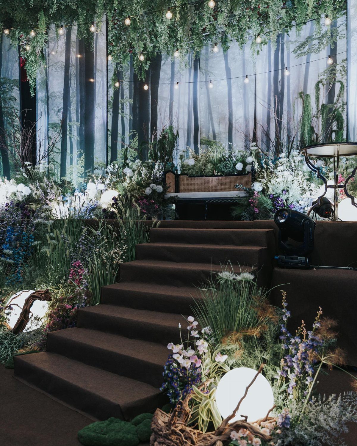 Dark stairs surrounded by lush greenery, wildflowers, and glowing orb lights in a forest-themed event setting.