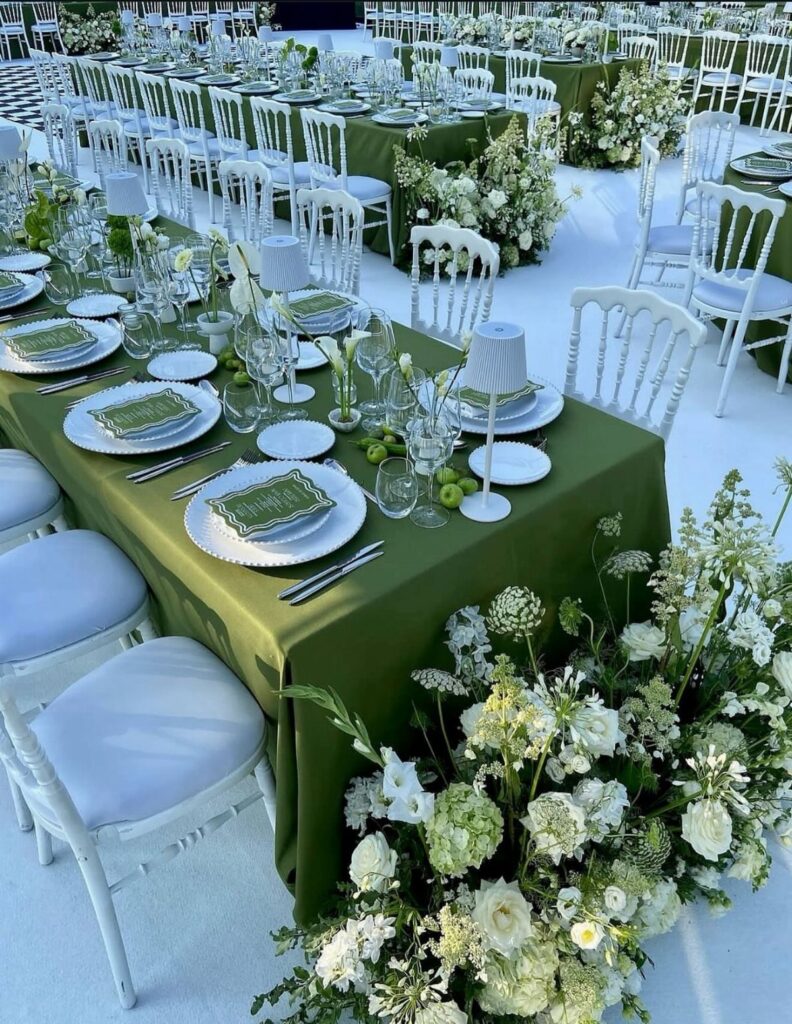 Long banquet tables with olive green linens, white plates, and lush white floral arrangements.