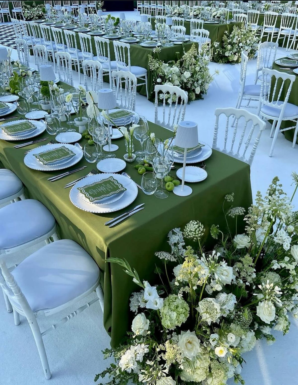 Long banquet tables with olive green linens, white plates, and lush white floral arrangements.