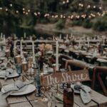 Rustic wedding table setting with a wooden sign that reads The Shire under string lights.