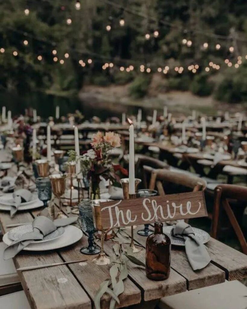 Rustic wedding table setting with a wooden sign that reads The Shire under string lights.