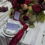 Wedding table setting with burgundy flowers, a gold goblet, and a patterned plate on white linen.