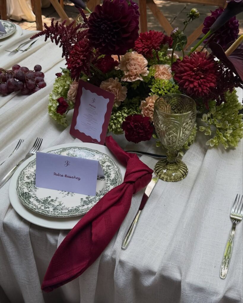 Wedding table setting with burgundy flowers, a gold goblet, and a patterned plate on white linen.