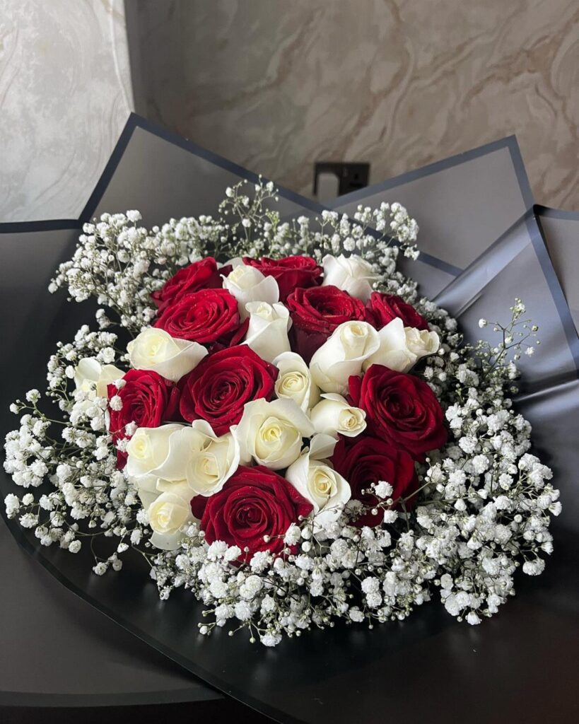 Red and white roses surrounded by delicate white baby's breath in a dark wrap.