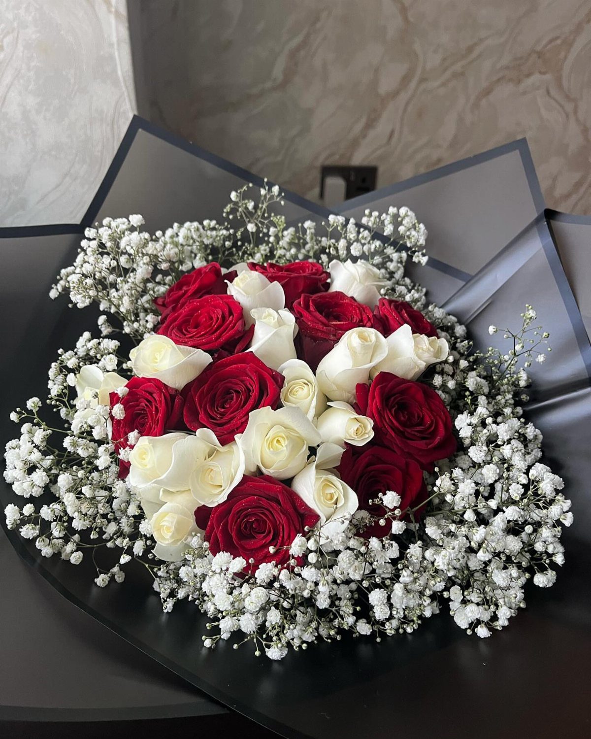 Red and white roses surrounded by delicate white baby's breath in a dark wrap.