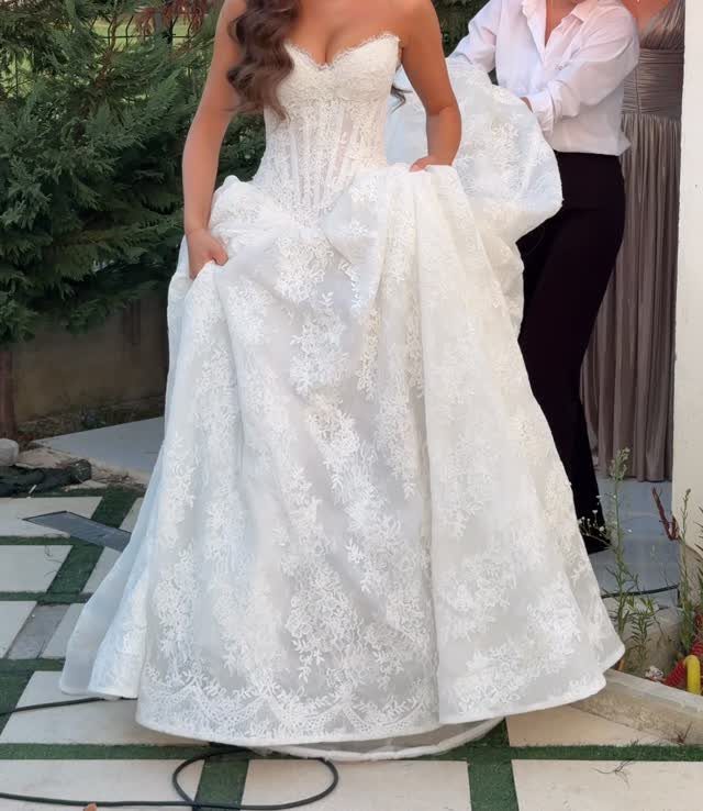 Woman wearing a white strapless lace wedding dress with a voluminous skirt standing outdoors.