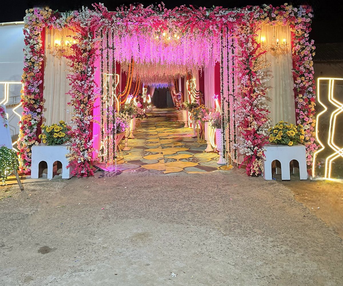 Floral wedding entrance tunnel with pink and white flowers, hanging blossoms, and glowing chandeliers.